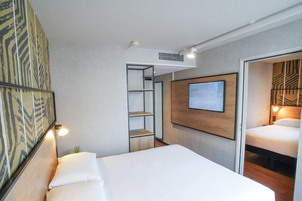 Una habitación de hotel moderna con una cama, un televisor montado en la pared, una planta pequeña y un papel tapiz estampado.
