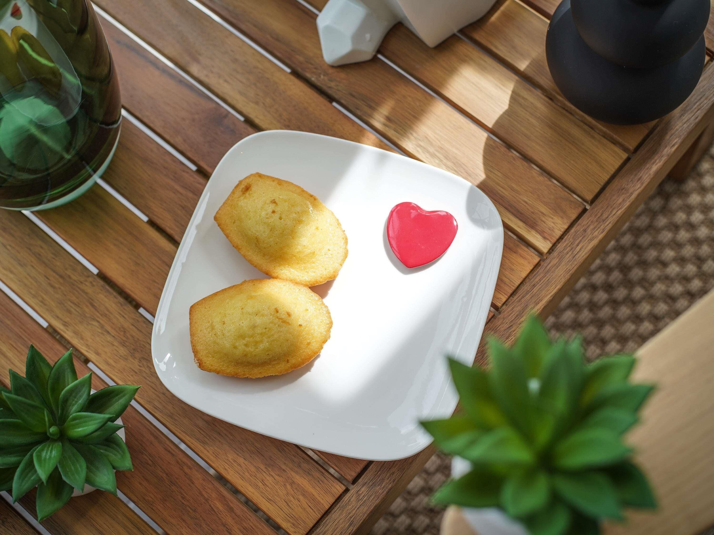 A white plate with two golden-brown pastries and a red heart-shaped decoration on a wooden table.