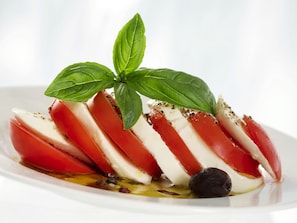 A plate of sliced mozzarella and tomato with a basil leaf garnish.