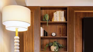 Een moderne woonkamer met een houten boekenkast, een comfortabele fauteuil, een rond bijzettafeltje en een grote lamp.