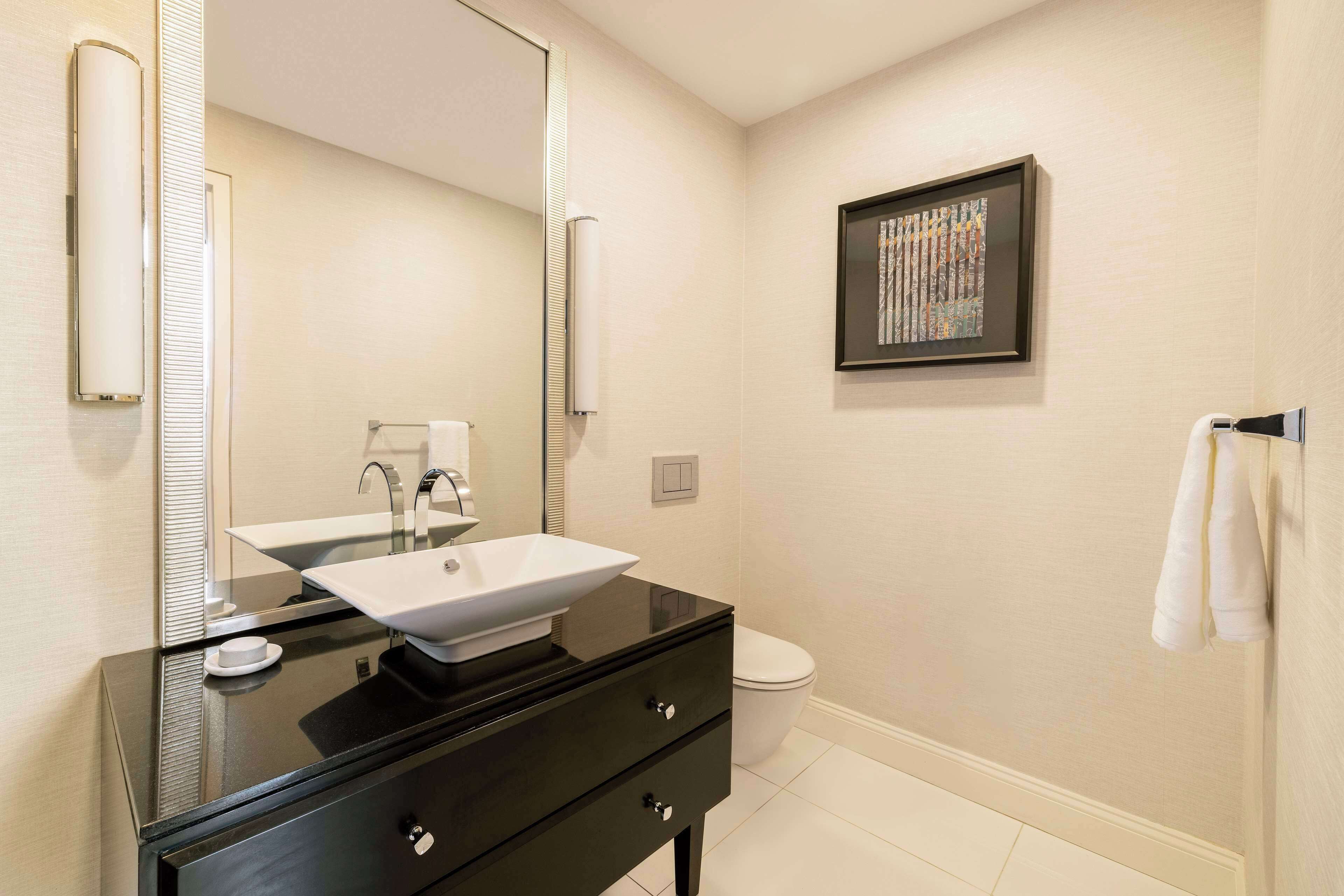 A modern bathroom with a black vanity, a white sink, and a framed artwork on the wall.