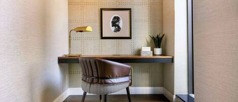 A corner office with a desk, chair, framed artwork, lamp, and potted plant.