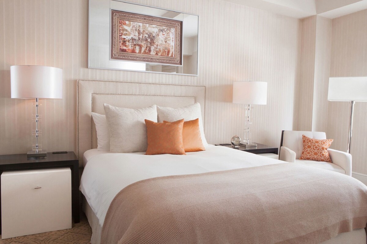 A hotel room with a large bed, two bedside tables, a chair, a small cabinet, and a painting on the wall.