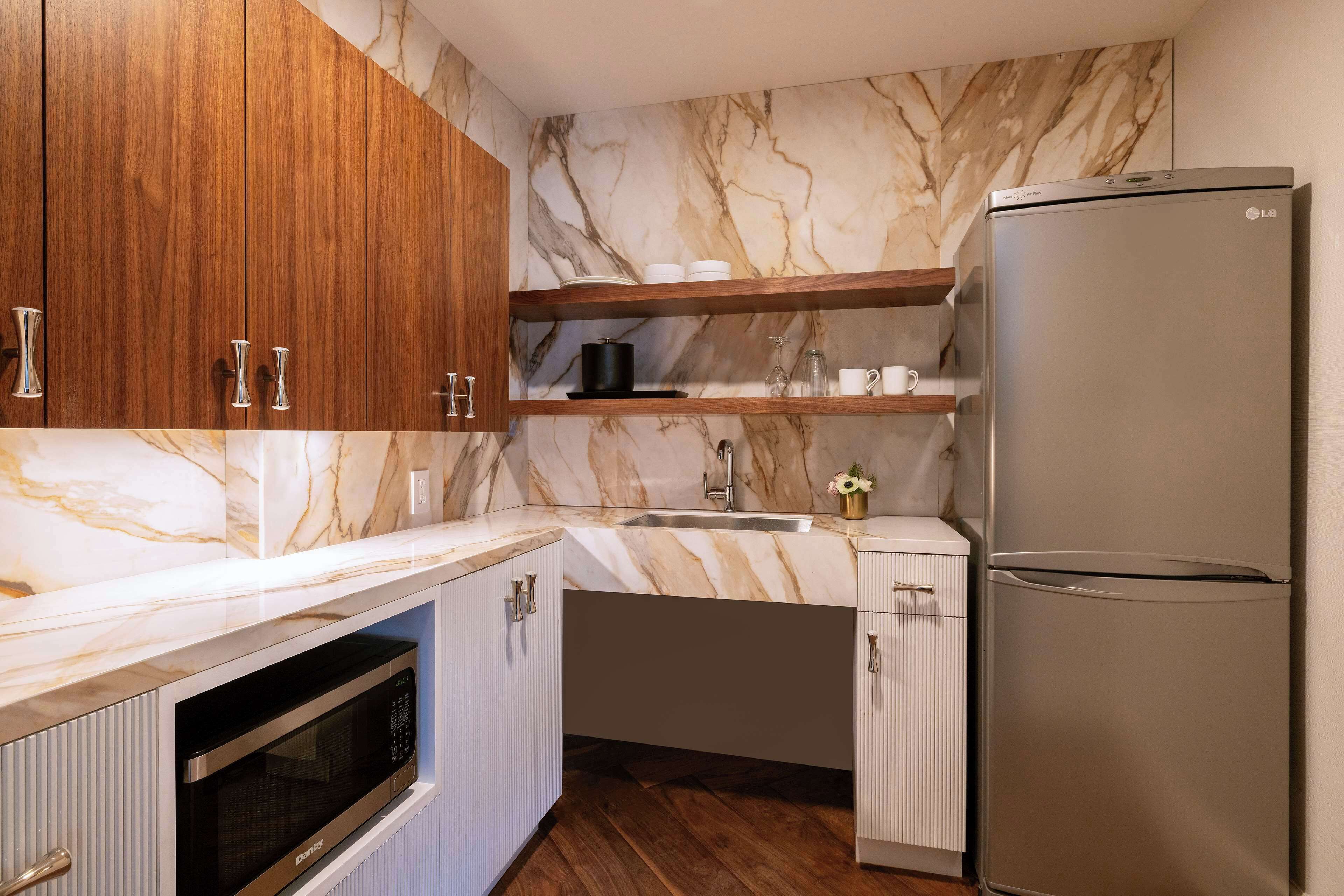 A kitchen with wooden cabinets, a marble backsplash, a stainless steel refrigerator, and a built-in oven.