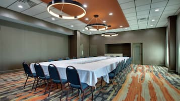 Sala de conferências com uma mesa comprida, cadeiras e luminárias modernas.