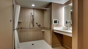 A modern bathroom with a walk-in shower, grab bars, a toilet, and a sink with a mirror.