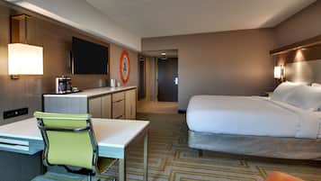Una habitación de hotel con cama, escritorio con silla, televisor y cafetera.