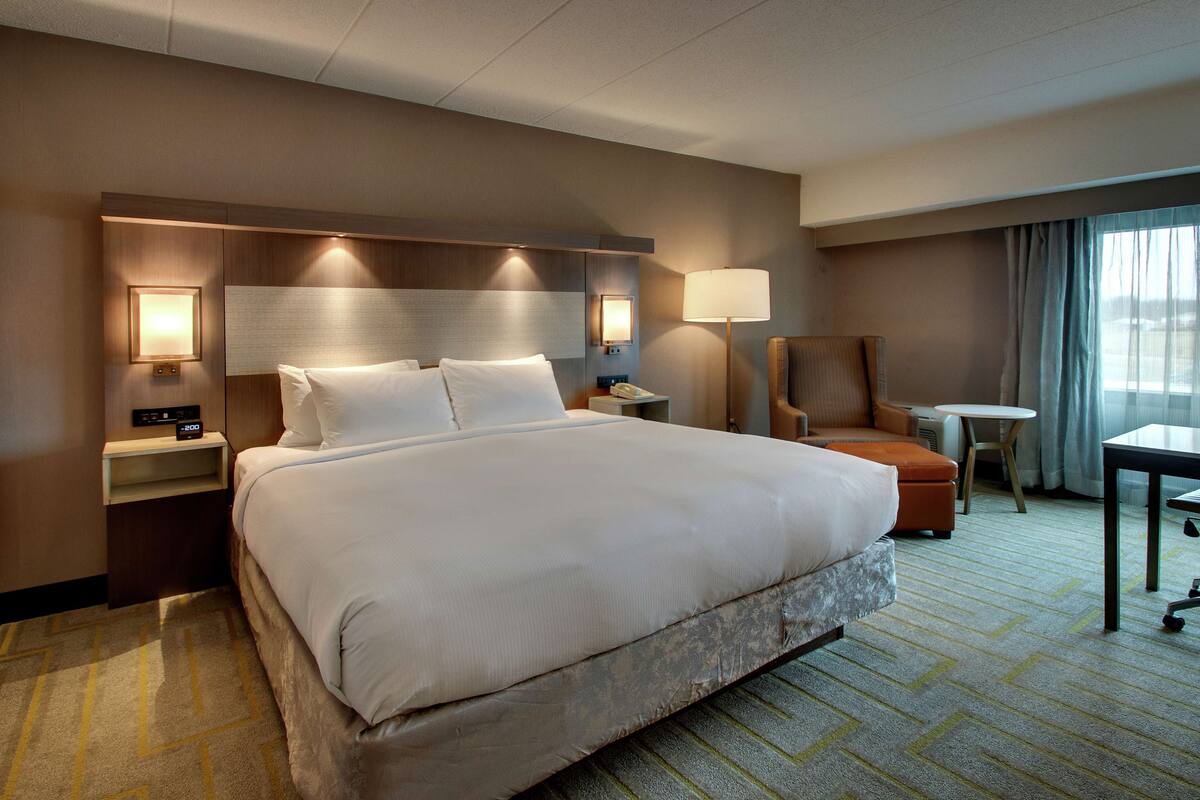 Une chambre d’hôtel avec un grand lit, des tables de chevet, un bureau, une chaise et une lampe.