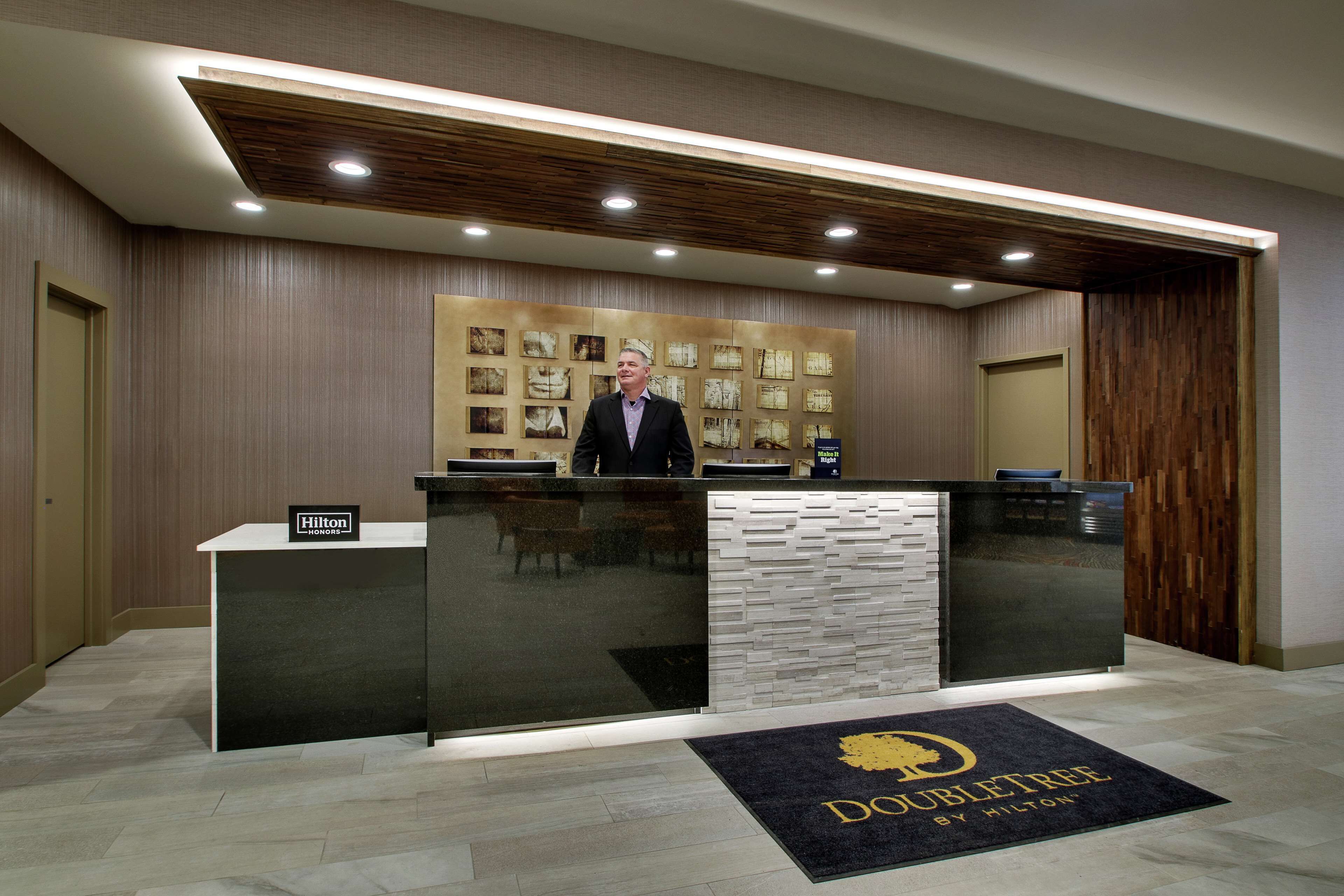 Ein moderner Hotelrezeptionstresen, eine Wandpaneele aus Holz mit gerahmten Bildern und ein Schild, das anzeigt, dass es sich um ein Hilton Honors Hotel handelt.