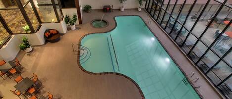 An indoor swimming pool with a tiled floor, surrounded by seating areas and potted plants.