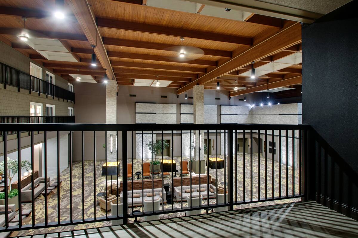 Un hall d’entrée spacieux avec un plafond haut, des poutres en bois et un tapis à motifs. On y trouve plusieurs coins salon avec des canapés et des fauteuils.