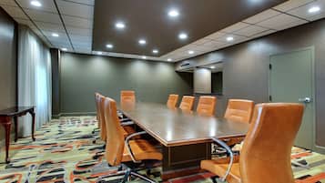 A conference room with a long table, eight chairs, a patterned carpet, and recessed ceiling lights.