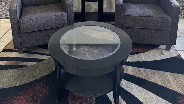 A lobby with two grey armchairs, a glass-top coffee table, and a painting of trees on the wall. - Quality Inn Forsyth - Decatur (Forsyth)
