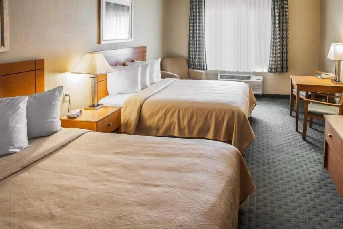 Habitación de hotel con dos camas, un escritorio, una silla, una lámpara y una ventana con cortinas.