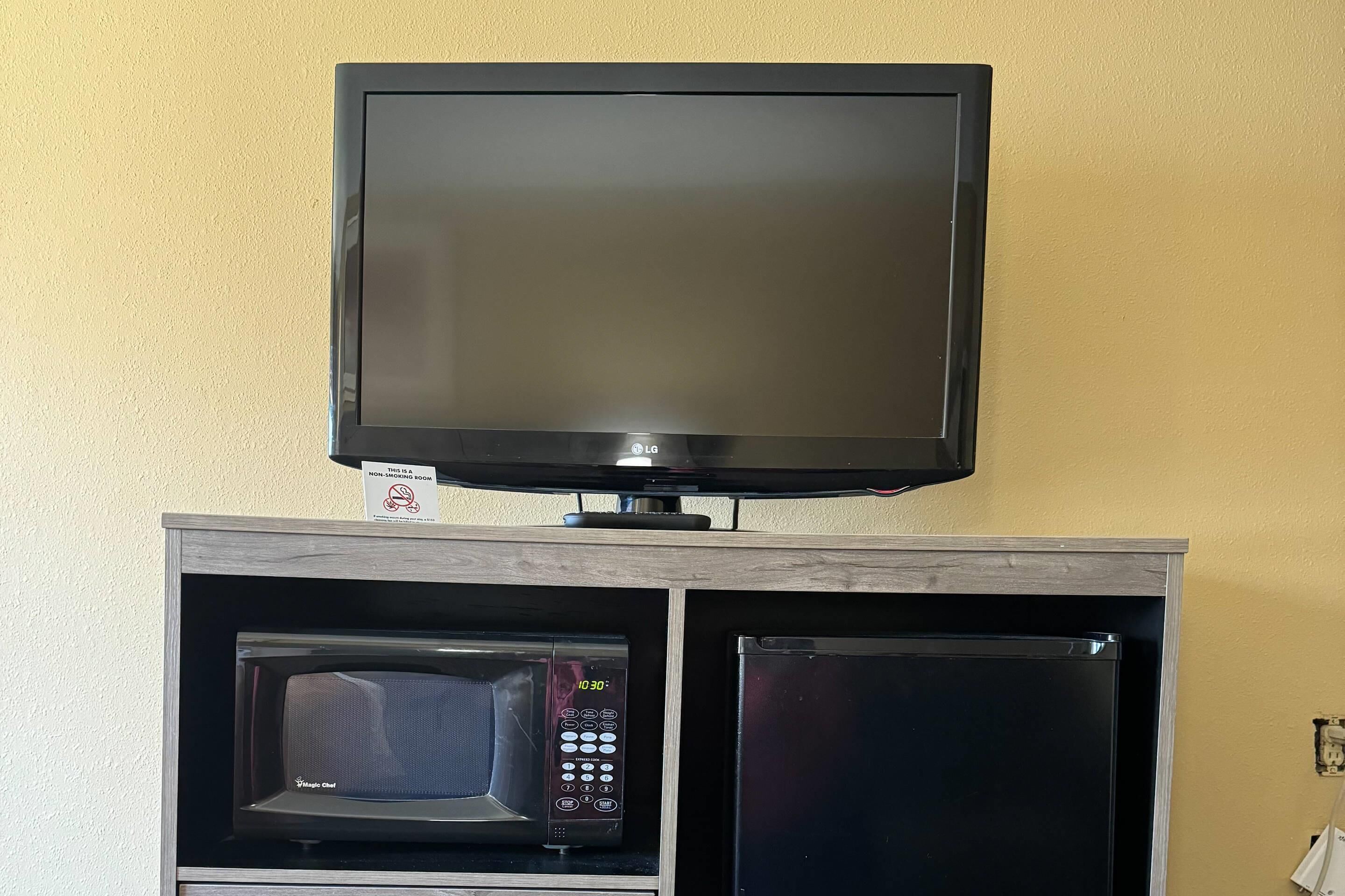 A television mounted on a wooden cabinet with a microwave and a refrigerator below it.