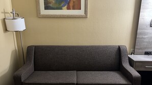 A modern room with a grey sofa, a wooden coffee table, a lamp, and a framed abstract painting on the wall. - Quality Inn Forsyth - Decatur (Forsyth)