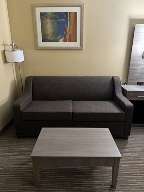 A modern room with a grey sofa, a wooden coffee table, a lamp, and a framed abstract painting on the wall. - Quality Inn Forsyth - Decatur (Forsyth)