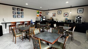 A dining area with multiple tables and chairs, a kitchen area with appliances, and framed artwork on the walls. - Quality Inn Forsyth - Decatur (Forsyth)