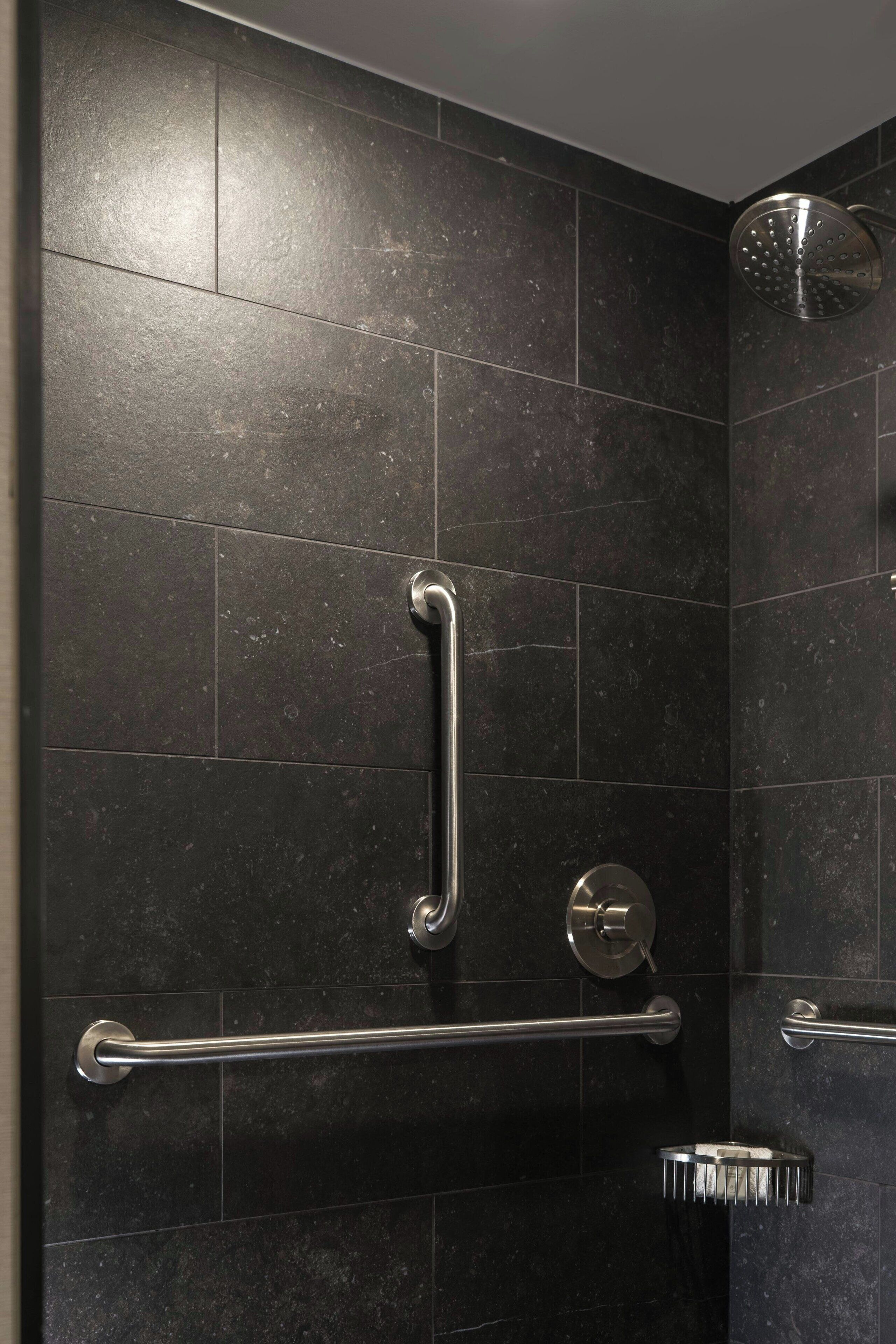 A modern shower with a handheld showerhead, grab bars, and a towel rack.