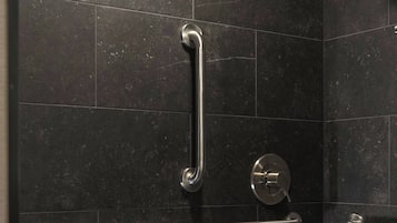 A modern shower with a handheld showerhead, grab bars, and a towel rack.