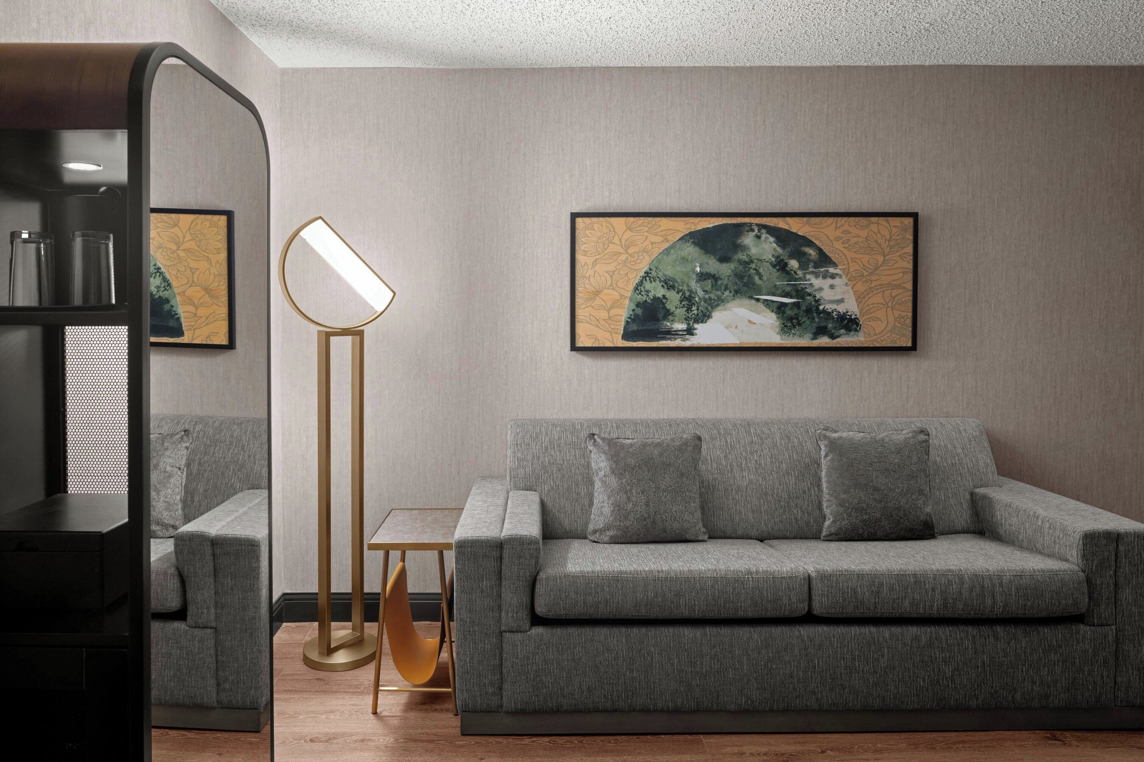 Una sala de estar moderna con un sofá gris, una lámpara de pie y obras de arte enmarcadas en la pared.