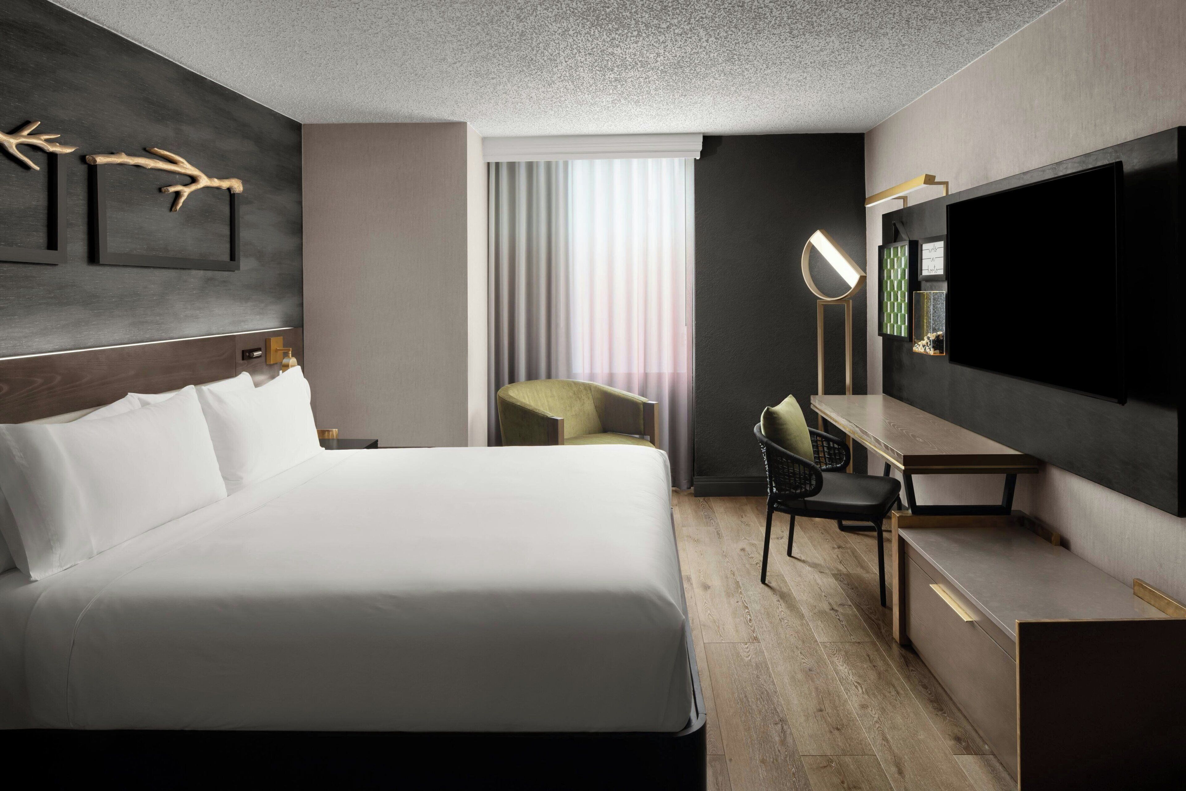 A hotel room with a large bed, a desk, a chair, a television, and a window with curtains.