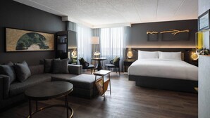 Une chambre d’hôtel moderne comprenant un canapé d’angle, une table basse ronde, un lit et un bureau avec une lampe.
