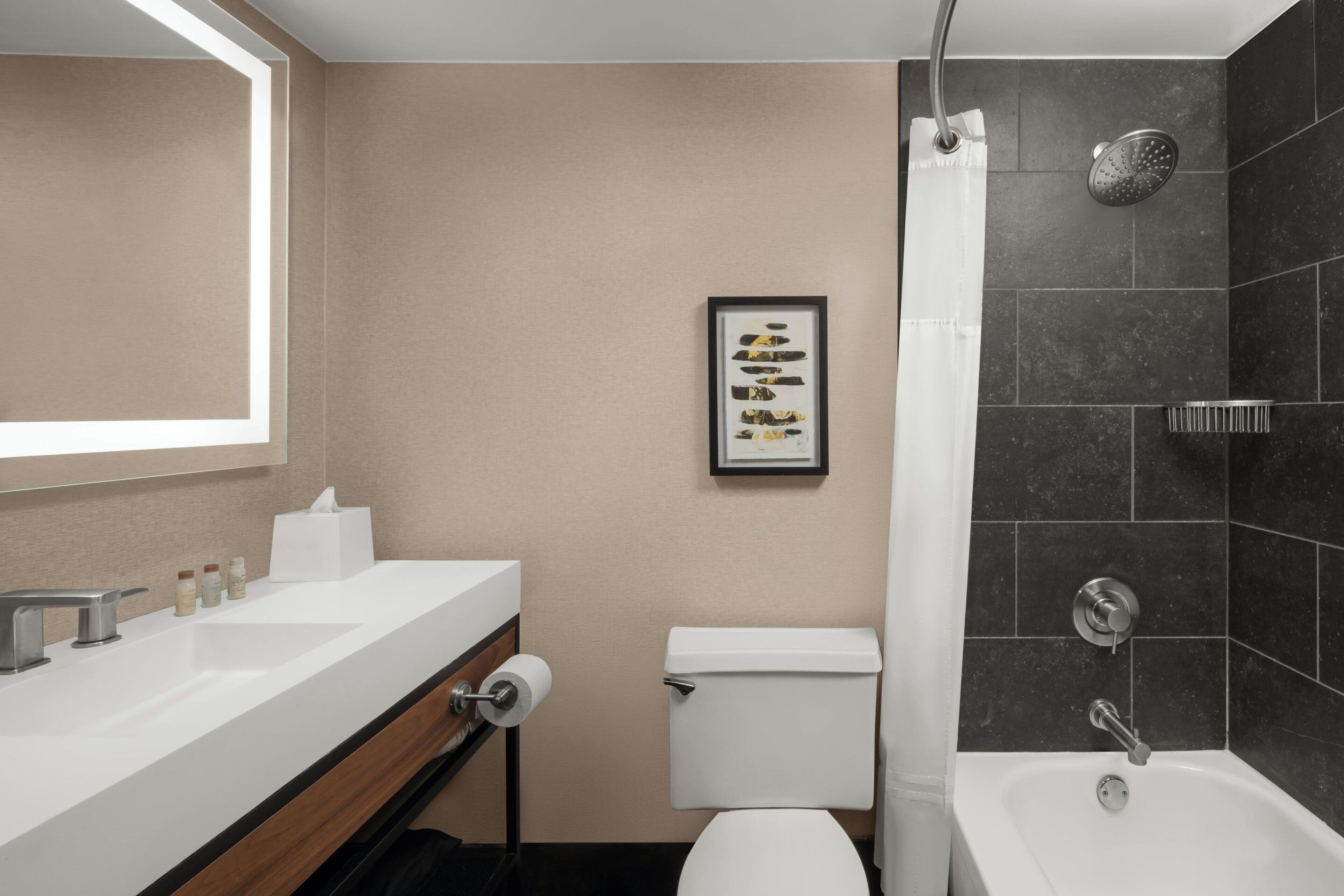 A modern bathroom with a white sink, toilet, and bathtub. There is a framed picture on the wall and a showerhead above the bathtub.