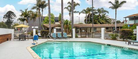 A swimming pool with lounge chairs, palm trees, and a building in the background.
