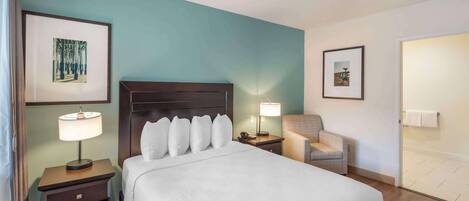 A hotel room with a large bed, a nightstand with a lamp, a chair, and two framed pictures on the walls.