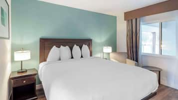 Ein Hotelzimmer mit einem großen Bett, einem Nachttisch mit Lampe, einem Sessel und Blick ins Freie durch ein Fenster.