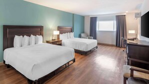 Habitación de hotel con dos camas, un escritorio, una silla, un televisor y una ventana con cortinas.