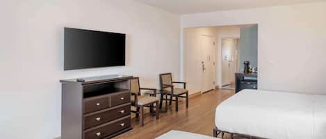 A hotel room with a bed, a desk with drawers, a television, and two chairs.