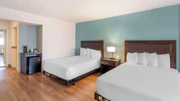 Ein Hotelzimmer mit zwei Betten, einem Schreibtisch mit Kaffeemaschine und einem kleinen Kühlschrank.