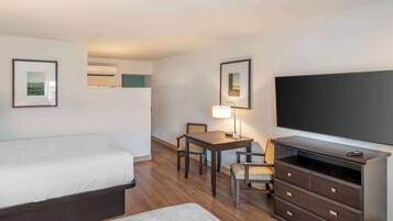 A hotel room with a bed, a desk with a chair, a dresser, and a flat-screen TV.