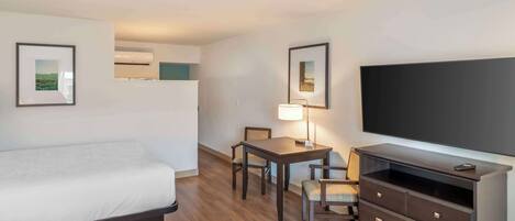 A hotel room with a bed, a desk with a chair, a dresser, and a flat-screen TV.