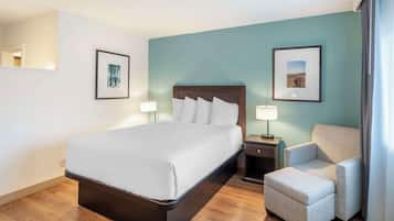 A hotel room with a bed, a chair, and two framed pictures on the walls.