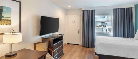 A hotel room with a bed, a desk with a lamp, a television, and a view of the outside.