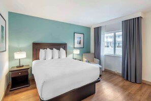 A hotel room with a large bed, a chair, a nightstand, a window with curtains, and a teal wall. - Best Western at Ventura Pier (Ventura)