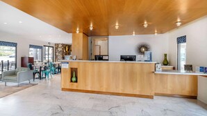 Un área de recepción moderna con un mostrador de madera, suelo de mármol y vistas al estacionamiento.