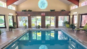 Una piscina interior amb pared de maó, plantes en testos i un fanal circular.