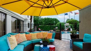 An outdoor seating area with a yellow umbrella, a pool, and a sign indicating the area is open.