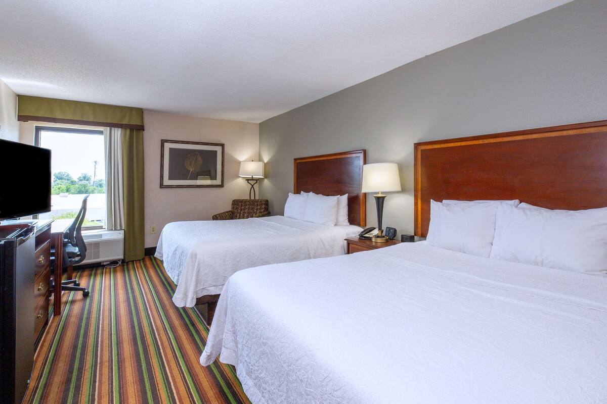 A hotel room with two beds, a desk with a chair, a television, and a window with curtains.