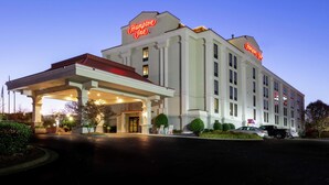 A Hampton Inn hotel with a covered entrance, multiple floors, and a well-lit facade.