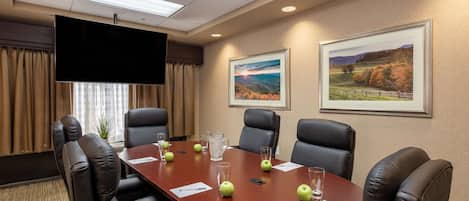 A conference room with a long table, leather chairs, a flat-screen TV, and framed landscape pictures on the wall.