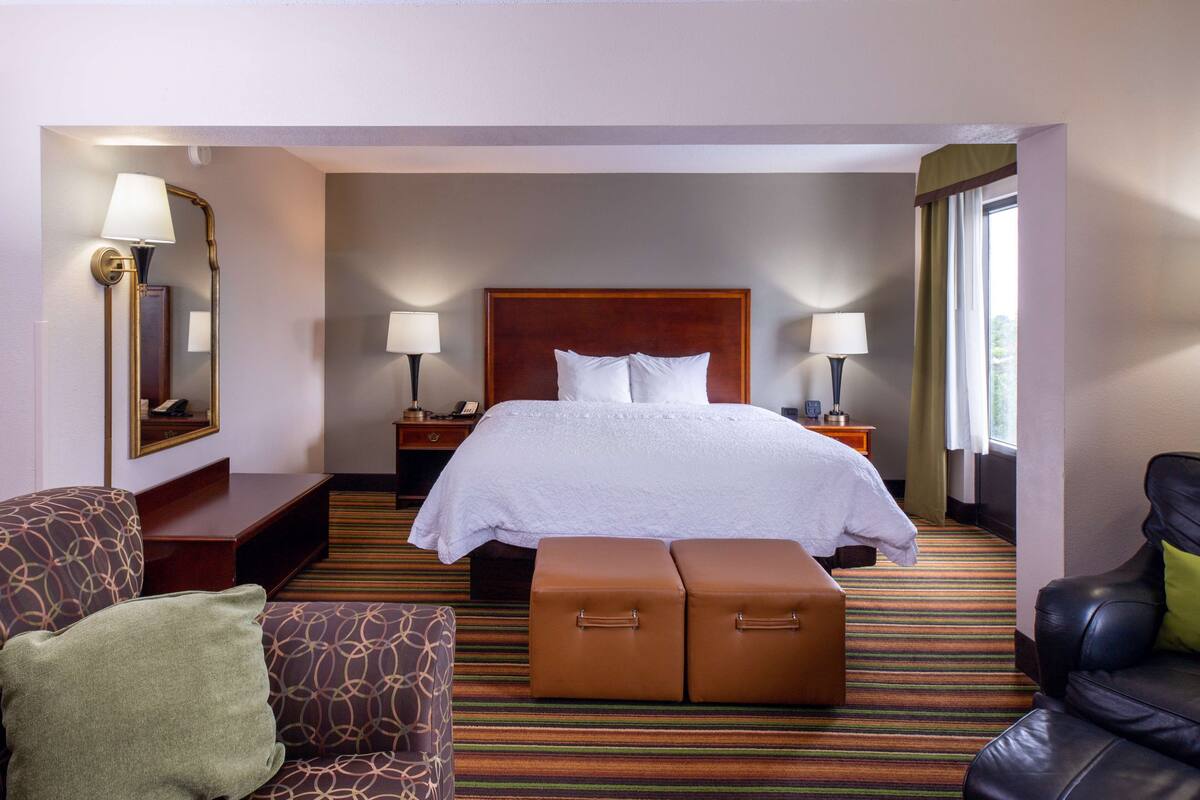 A hotel room with a large bed, two bedside tables, a chair, a sofa, a small table, and a window with curtains.