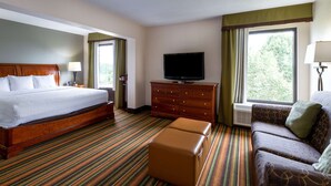 A hotel room with a large bed, a sofa, a television on a wooden cabinet, and a window with curtains.