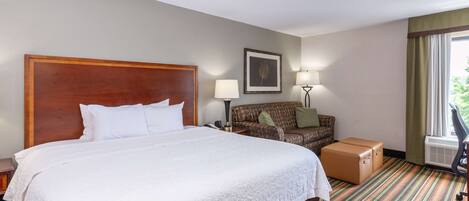 Una habitación de hotel con una cama grande, un sofá, un escritorio, una lámpara y una ventana con cortinas.