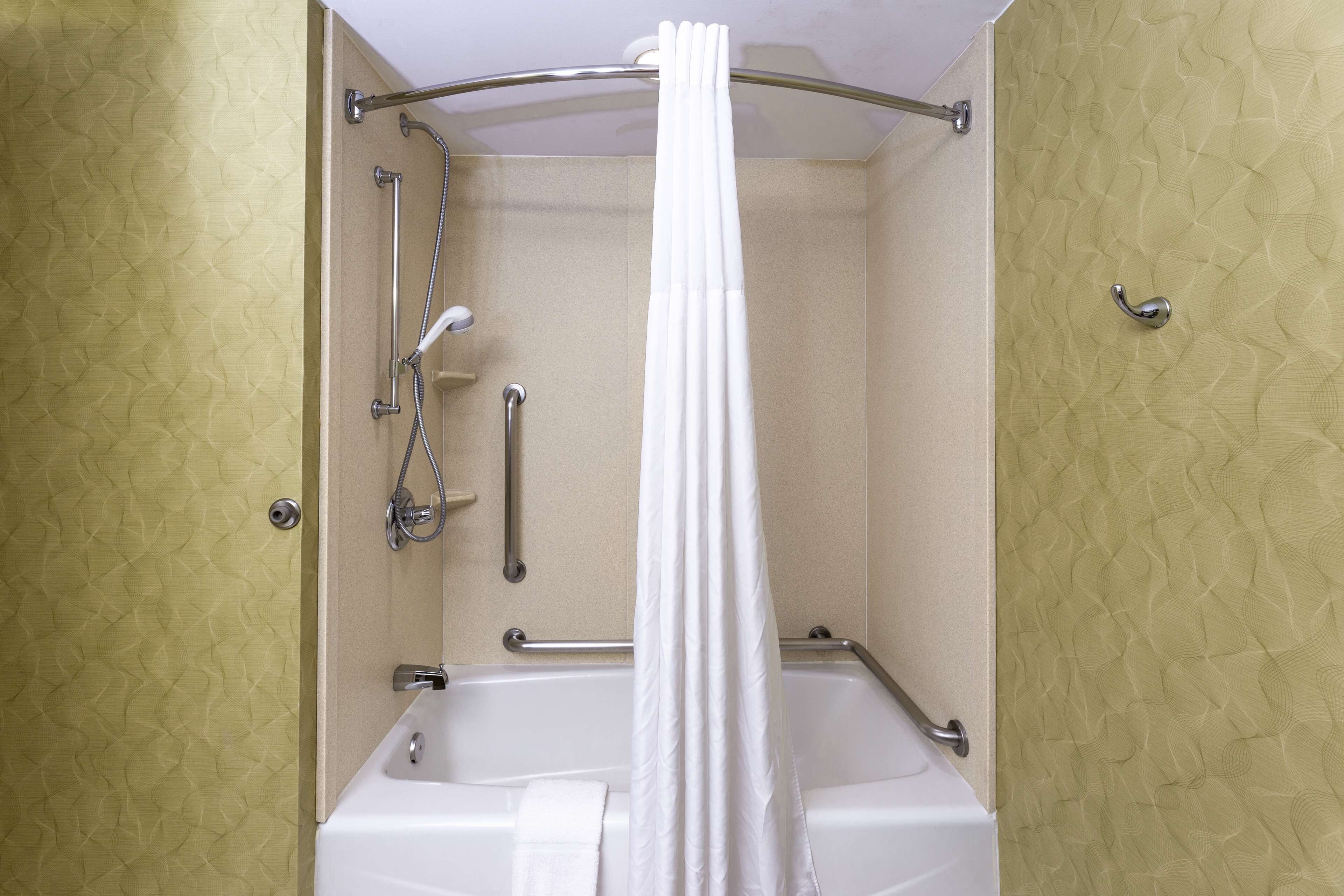 A bathroom with a bathtub, shower, and handrails.
