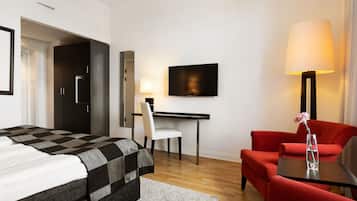 A hotel room with a bed, a desk, a TV, a chair, and a red armchair.